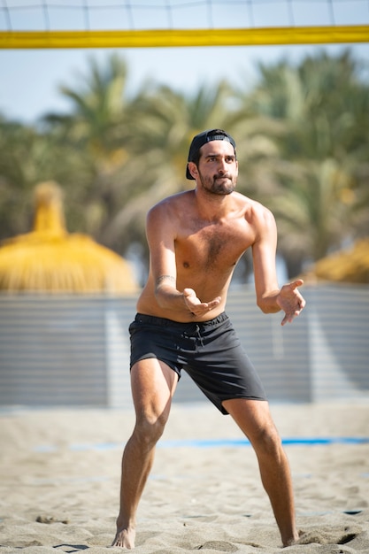 Photo jeune homme jouant au beach-volley sur la plage par une journée ensoleillée