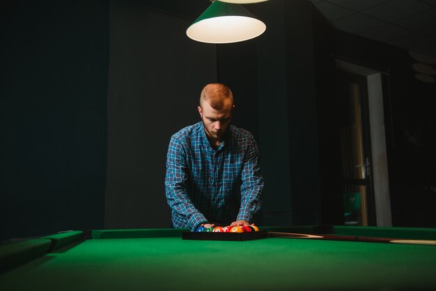 Jeune homme jouant au billard dans le club de billard sombre