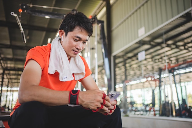 Photo jeune homme jouant au téléphone et écoutant de la musique après l'exercice avec divers équipements d'exercice en fitness