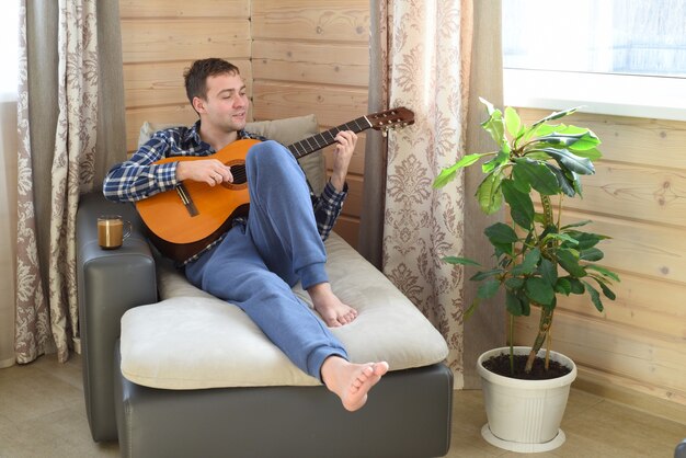 Jeune homme jouant de la guitare et assis sur un canapé