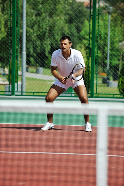 Un jeune homme joue au tennis à l'extérieur.