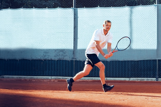 Jeune homme joue au tennis en plein air sur un court de tennis en terre battue le matin