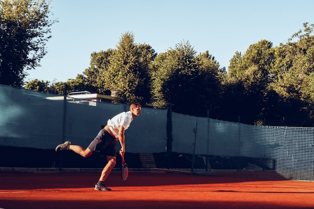 Jeune homme joue au tennis en plein air sur un court de tennis en terre battue le matin