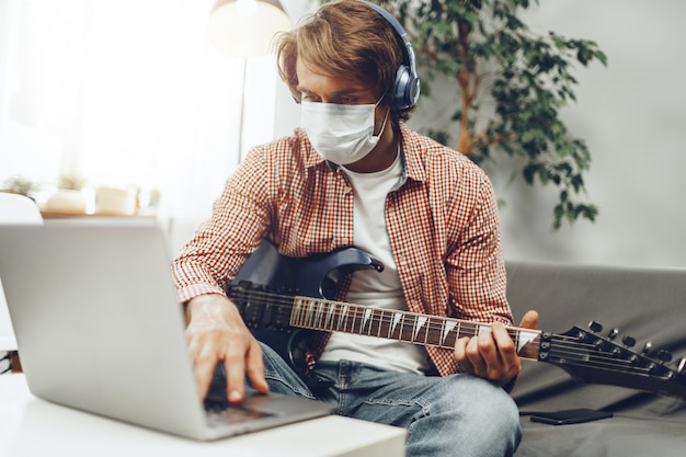 Jeune homme joue de la guitare à la maison en masque médical