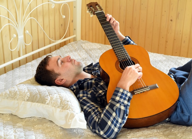 Jeune homme, jouer guitare, et, poser, lit