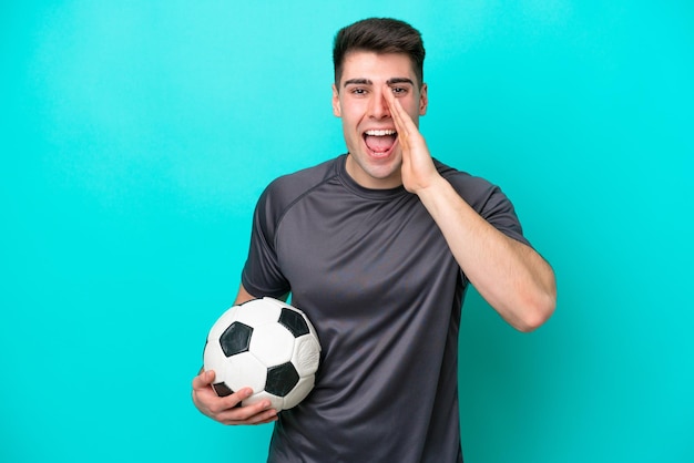 Jeune homme de joueur de football caucasien isolé sur fond bleu criant avec la bouche grande ouverte