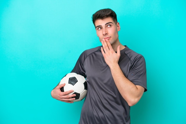 Jeune homme de joueur de football caucasien isolé sur fond bleu levant les yeux en souriant