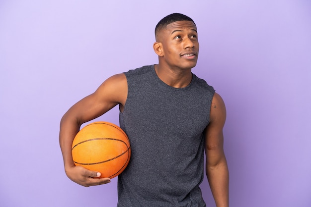 Jeune homme de joueur latin de basket-ball isolé pensant une idée tout en levant les yeux