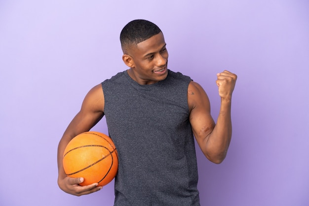 Jeune homme de joueur latin de basket-ball isolé sur violet célébrant une victoire