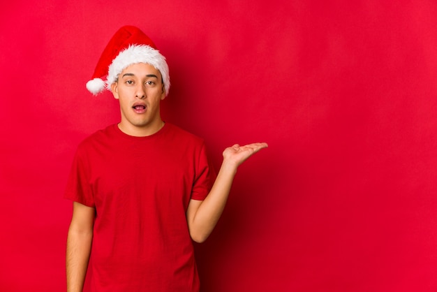 Jeune homme le jour de Noël impressionné tenant l'espace copie sur la paume.