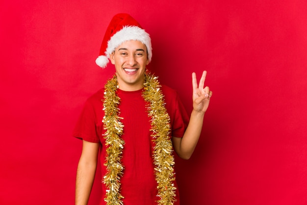 Jeune homme le jour de Noël joyeux et insouciant montrant un symbole de paix avec les doigts.