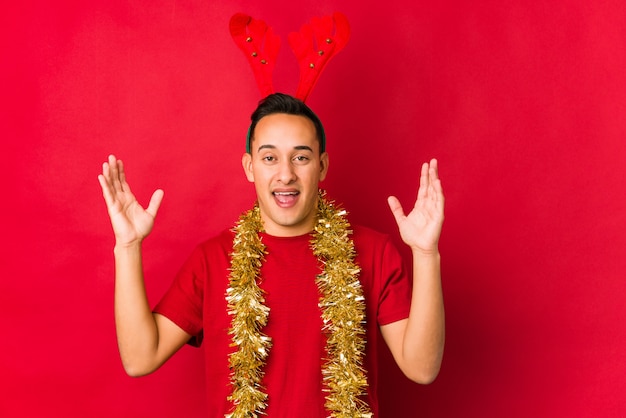 Jeune homme le jour de Noël recevant une agréable surprise, excité et levant les mains.