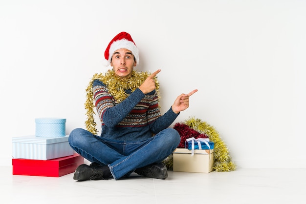 Jeune homme le jour de Noël souriant pointant gaiement avec l'index.