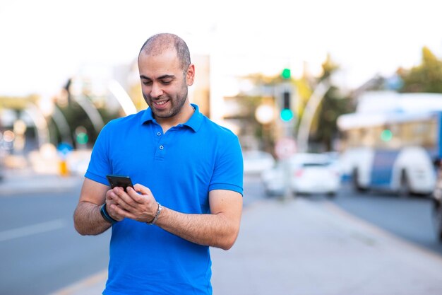 Jeune homme joyeux et confiant vérifiant ses e-mails et regardant son smartphone dans un espace urbain Comprend une copie et un espace de texte