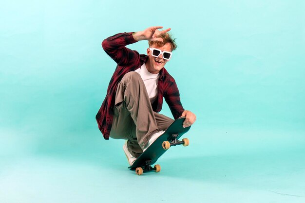 Photo un jeune homme joyeux fait du skateboard sur un fond bleu isolé, un patineur hipster.