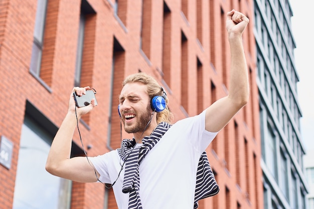 Un jeune homme joyeux et heureux écoute de la musique et danse dans la rue