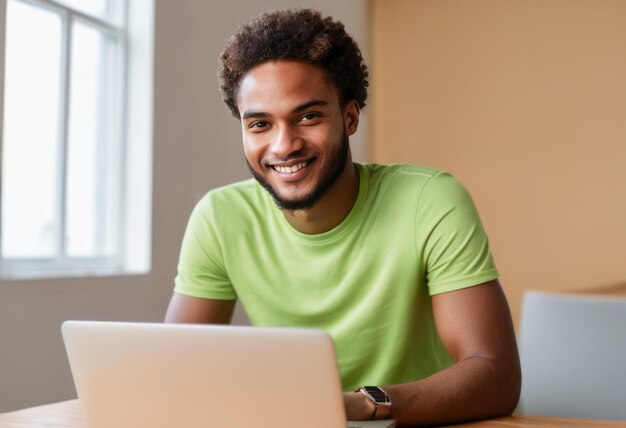 Jeune homme joyeux avec un sourire vif travaillant sur un ordinateur portable à la maison sa chemise verte reflète un détendu