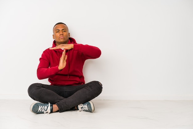 Jeune homme latin assis sur le sol montrant un geste de temporisation.