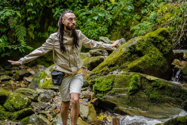 Jeune homme latin aux cheveux longs faisant silence pour écouter le son de la jungle