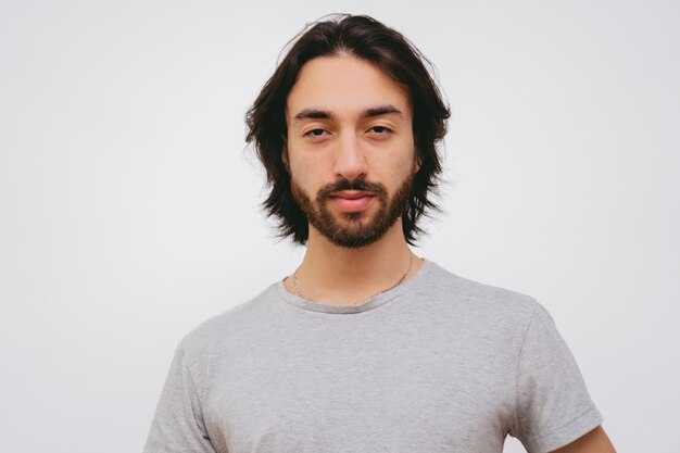 Jeune homme latin avec barbe et cheveux longs regardant la caméra souriant fond blanc