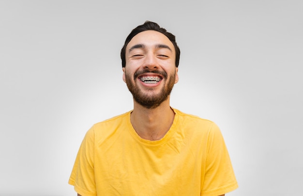 Jeune homme latin à bretelles souriant à la caméra fond blanc