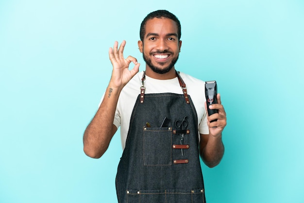 Jeune homme latin de coiffeur isolé sur fond bleu montrant un signe ok avec les doigts