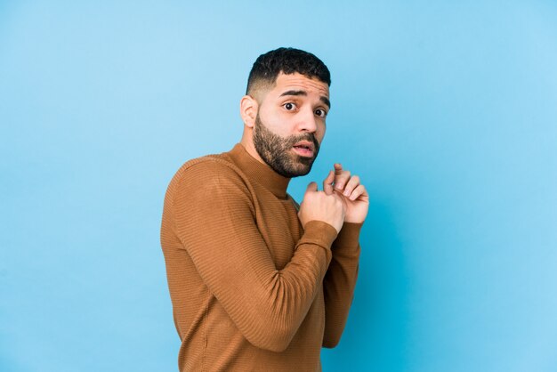 Jeune homme latin contre un mur bleu isolé, effrayé et effrayé.