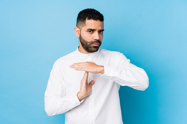 Jeune homme latin contre un mur bleu isolé montrant un geste de temporisation.