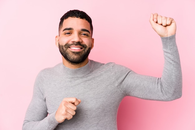 Jeune homme latin contre un mur rose dansant et s'amusant.