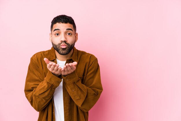 Jeune homme latin contre un mur rose isolé lèvres pliantes et tenant les paumes pour envoyer un baiser d'air.