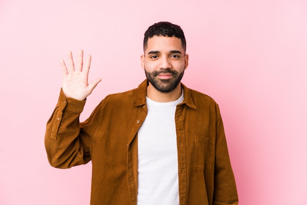 Jeune homme latin contre un mur rose isolé souriant joyeux montrant le numéro cinq avec les doigts.