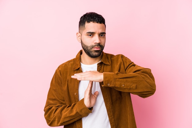 Jeune homme latin contre un rose isolé montrant un geste de temporisation.