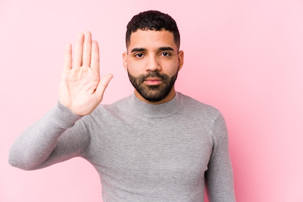 Jeune homme latin sur fond rose isolé debout avec la main tendue montrant le panneau d'arrêt, vous empêchant.