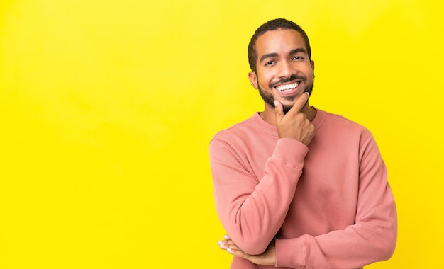 Jeune homme latin isolé sur fond jaune heureux et souriant