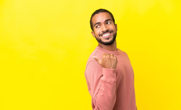 Jeune homme latin isolé sur fond jaune pointant vers le côté pour présenter un produit