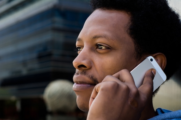 Jeune homme latin parle sur son téléphone portable à l&#39;extérieur.