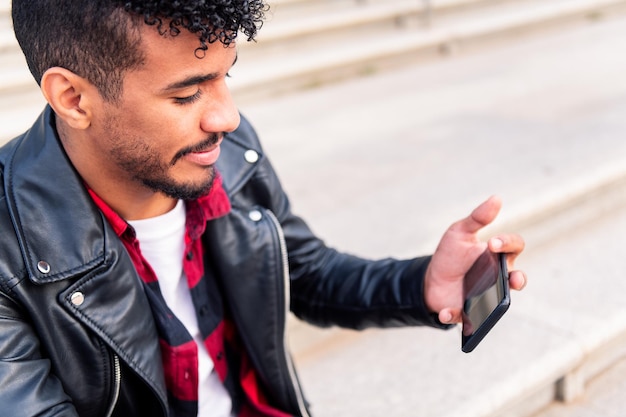 Jeune homme latin regardant une vidéo sur son téléphone intelligent, concept de technologie et mode de vie urbain