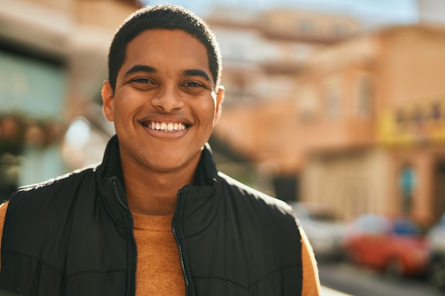 Jeune homme latin souriant heureux debout à la ville