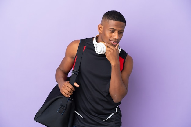 Jeune homme latin sport avec sac de sport isolé sur violet à la recherche sur le côté et souriant