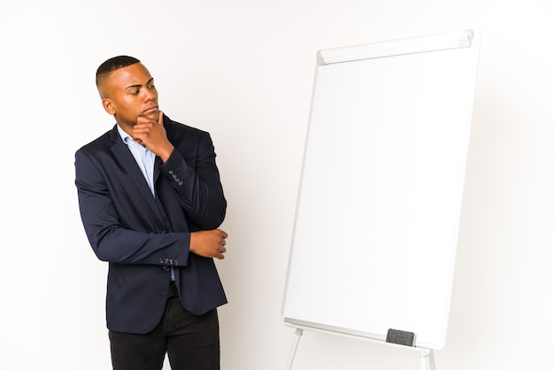 Jeune homme latin avec un tableau blanc isolé sur un espace blanc à la recherche de côté avec une expression douteuse et sceptique.