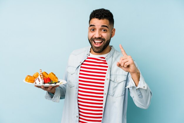 Jeune homme latin tenant une gaufre isolée ayant une idée, un concept d'inspiration.