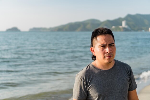 Jeune homme latino sérieux regardant sur le côté à la plage, concept de mode de vie urbain