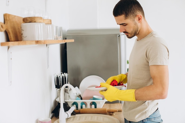 Un jeune homme lave la vaisselle dans la cuisine essuie une assiette