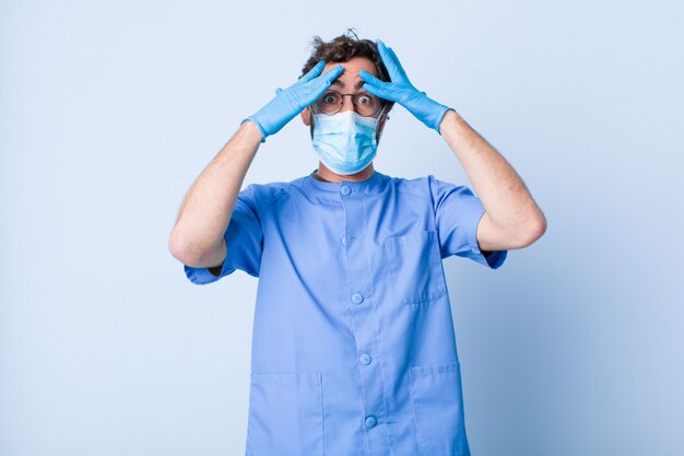 Jeune homme levant les mains à la tête, bouche bée, se sentant extrêmement chanceux, surpris, excité et heureux. concept de coronavirus