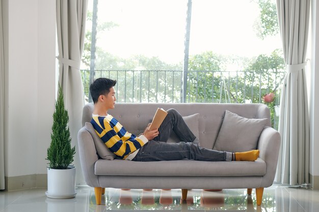 Jeune homme lisant un livre assis sur le canapé