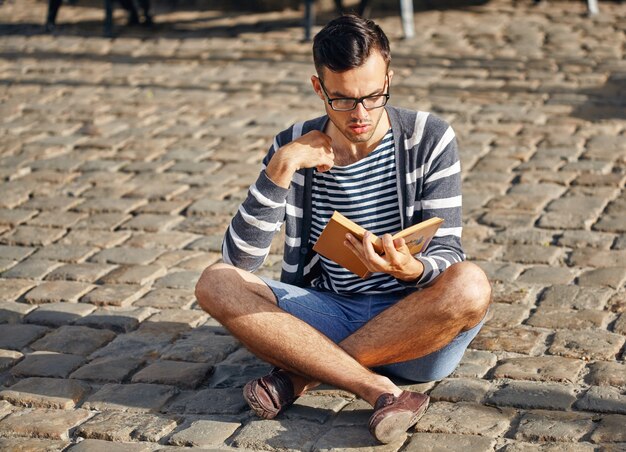 Jeune homme lisant un livre. Il s'assied sur le trottoir