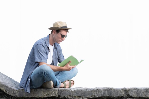 Jeune homme lisant un livre sur un mur de pierre. Étudier à l'extérieur pour les examens universitaires. Copiez l'espace.