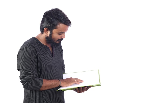 Jeune homme lisant ou tenant un livre ou un journal isolé sur un mur blanc.