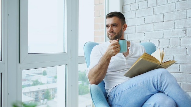 Un jeune homme lit un livre assis sur un balcon dans un appartement moderne