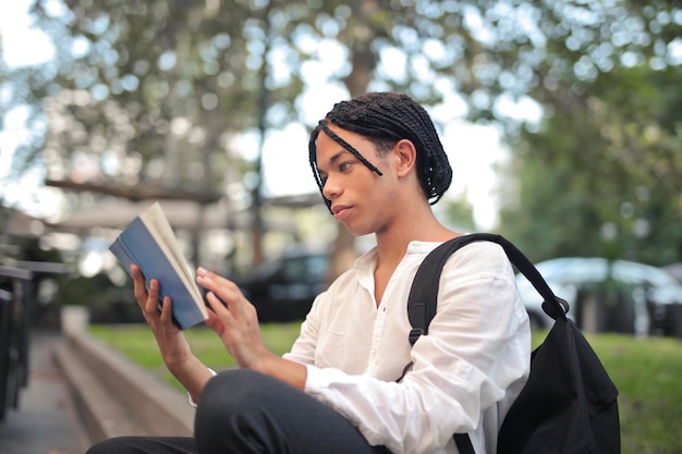 jeune homme lit un livre dans la rue